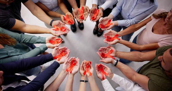 Flere mennesker, i en cirkel, med deres hænder udstrakt, hver med en rød sløjfe, symbol på rød december.